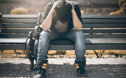 man in black shirt and gray denim pants sitting on gray padded bench