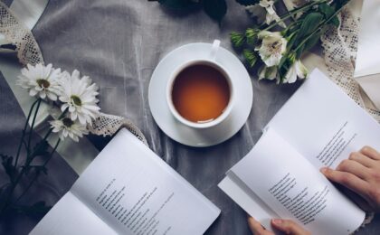 white ceramic teacup with saucer near two books above gray floral textile